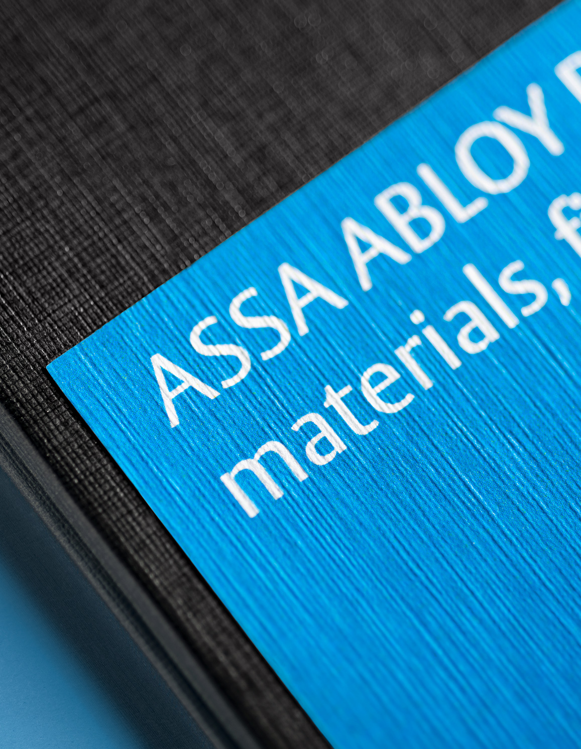 Dettaglio ravvicinato del cartoncino blu ASSA ABLOY con testo su texture nera goffrata