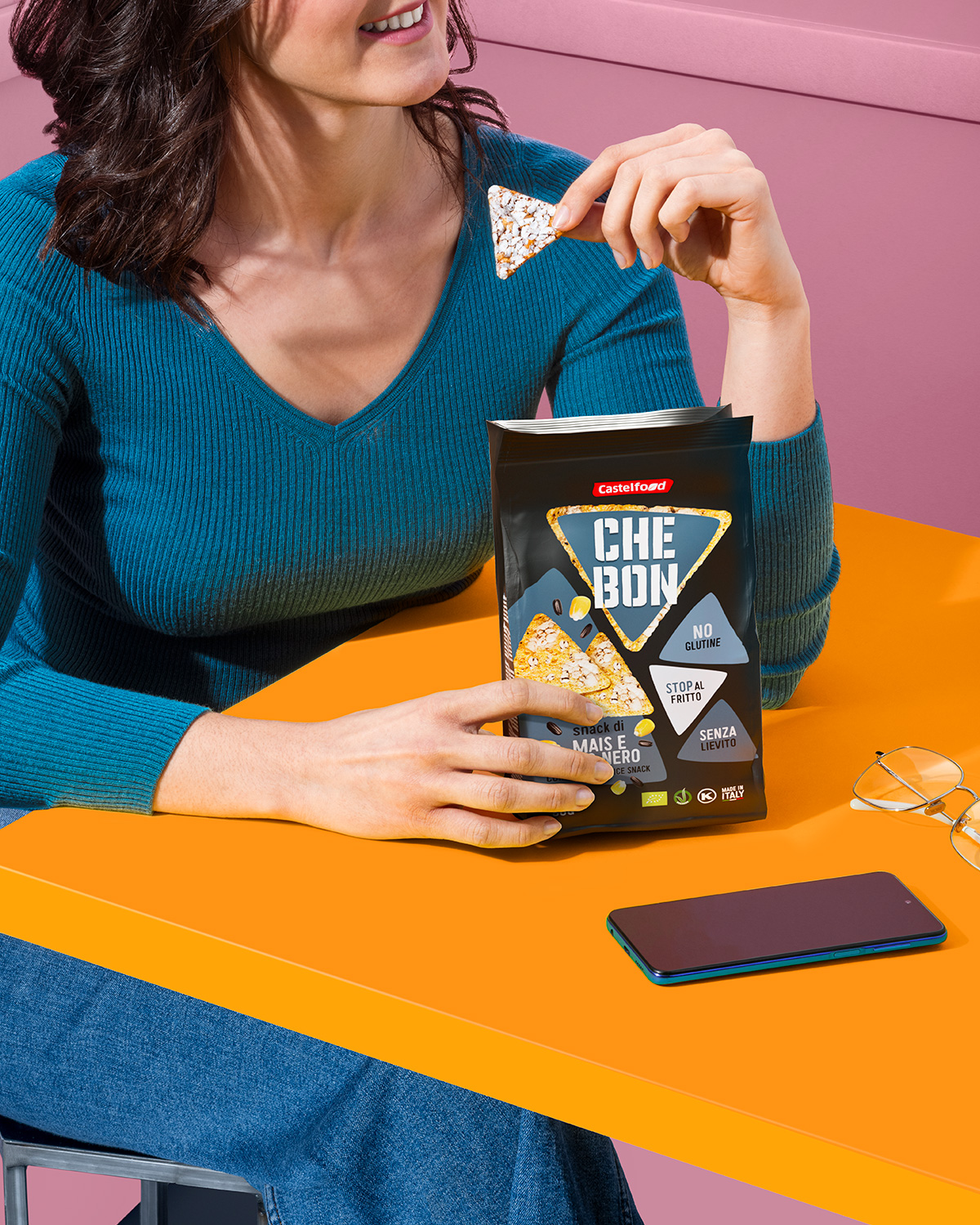 Donna seduta al tavolo mentre mangia uno snack triangolare Che Bon di Castelfood, confezione nera visibile