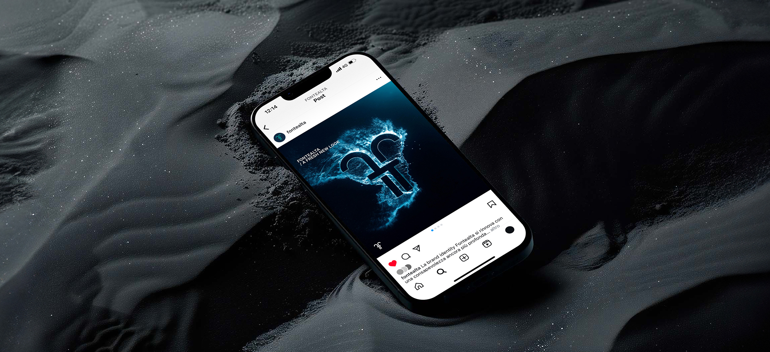 Smartphone appoggiato su una superficie sabbiosa nera che mostra un post Instagram del brand Fontealta con il logo illuminato da un effetto splash blu