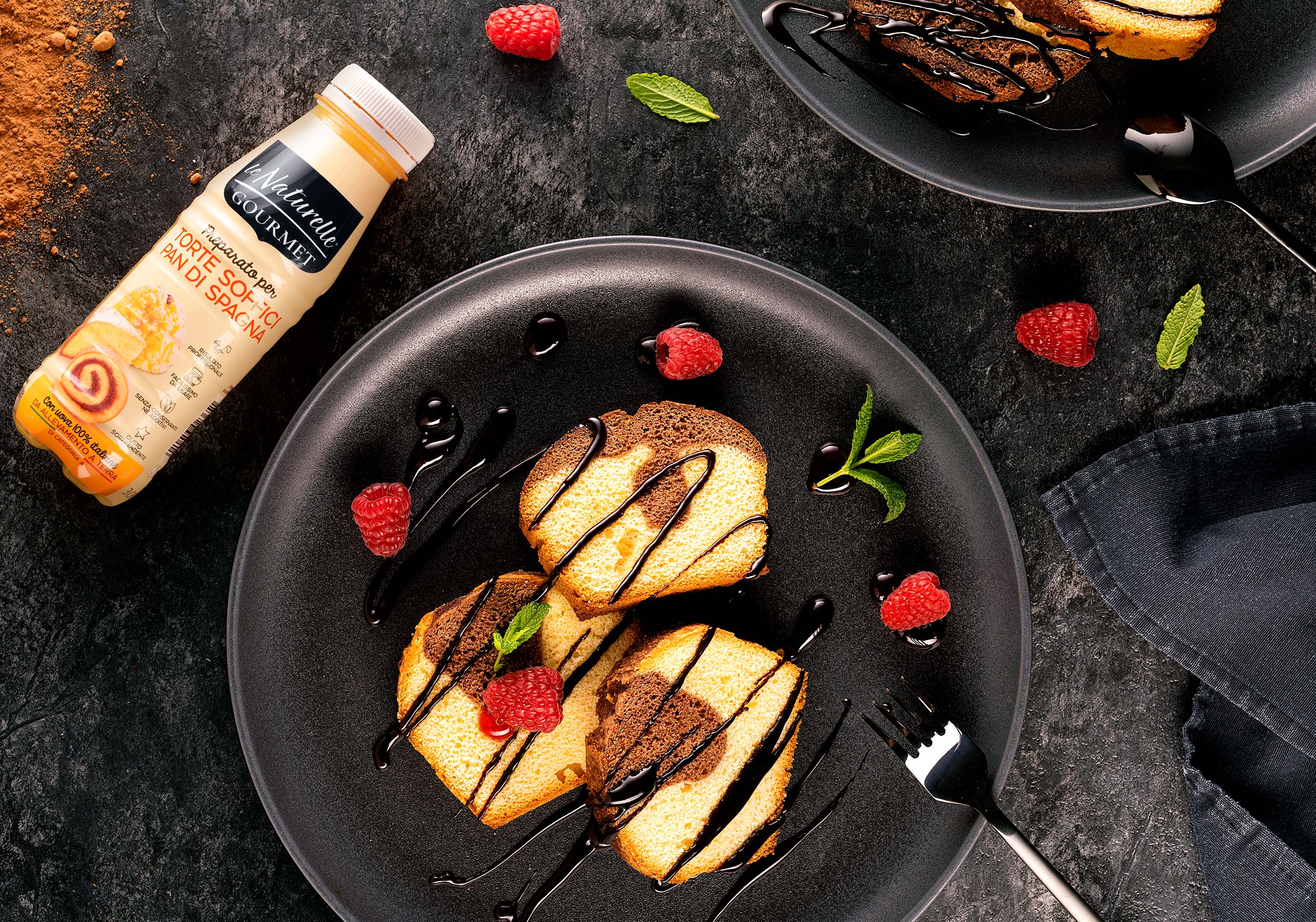 Fette di torta bicolore preparata con Le Naturelle Gourmet, guarnite con cioccolato e lamponi freschi
