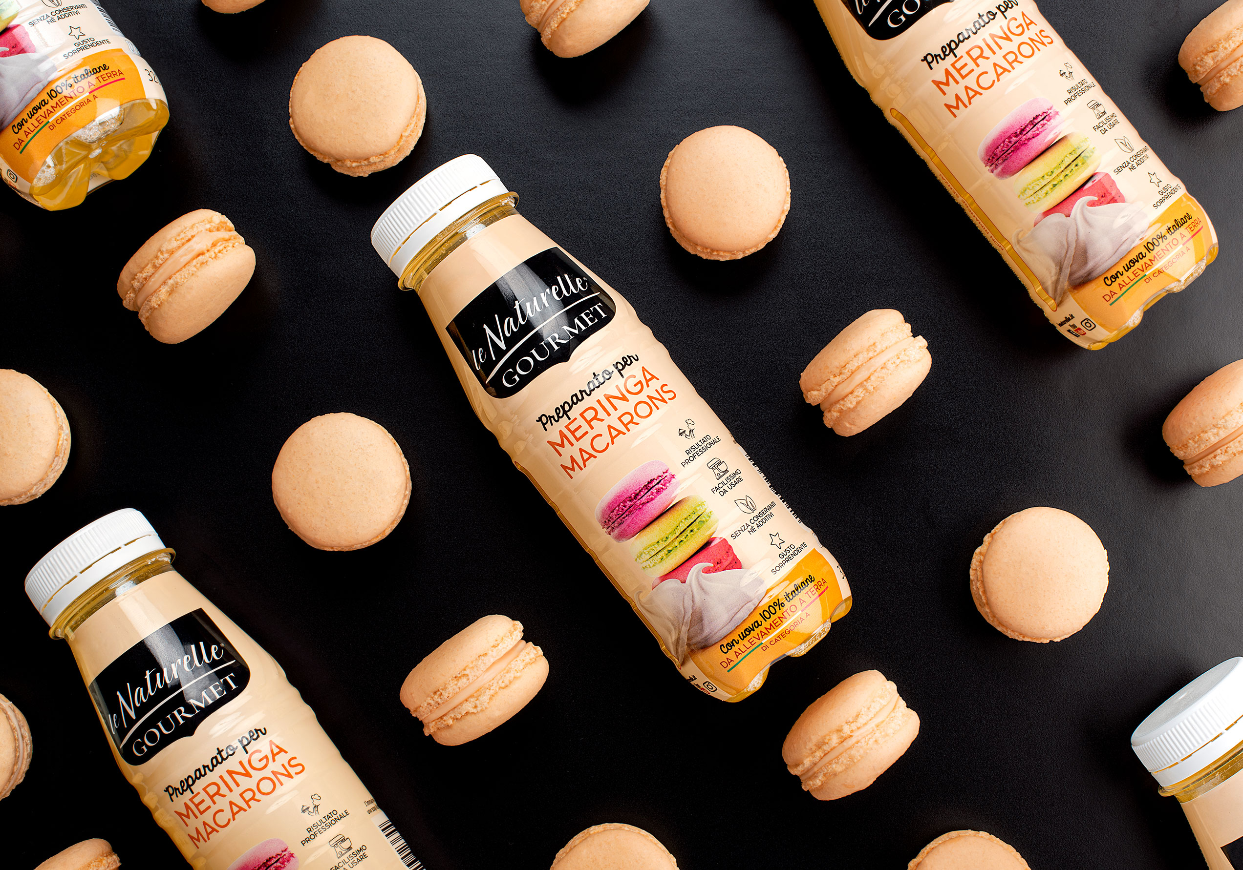 Macaron beige su fondo nero con bottiglia Le Naturelle Gourmet per Meringa e Macarons, preparato professionale con uova 100% italiane