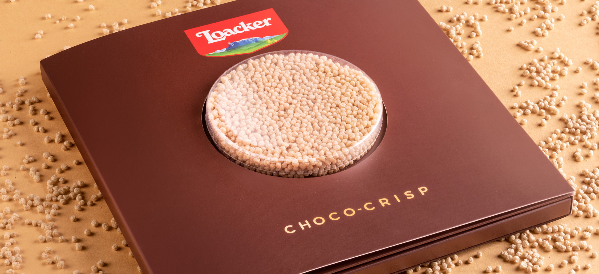 Packaging Loacker Choco-Crisp con finestrella tonda trasparente e wafer soffiato su sfondo beige