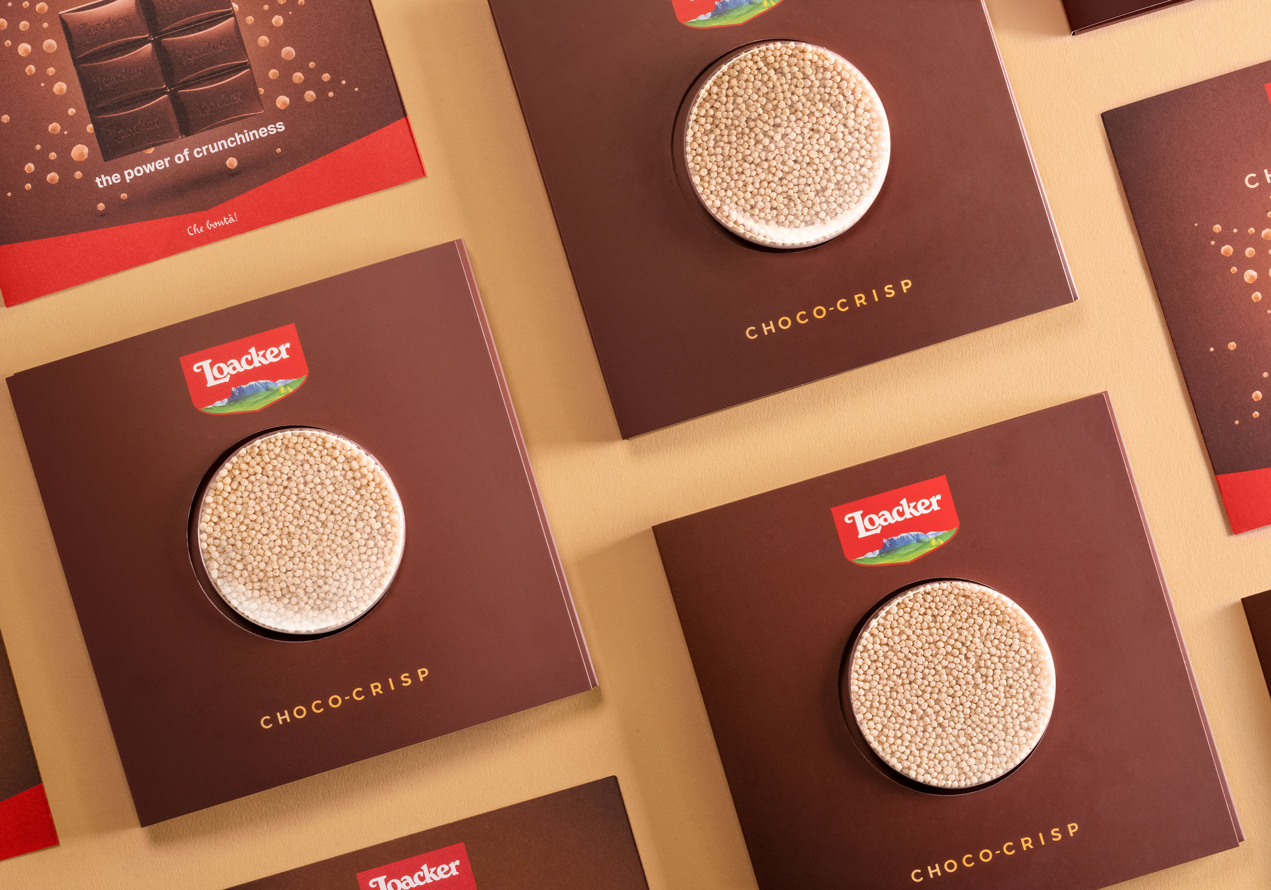 Vista dall’alto di più confezioni Loacker Choco-Crisp disposte su sfondo beige, con packaging marrone e logo in evidenza