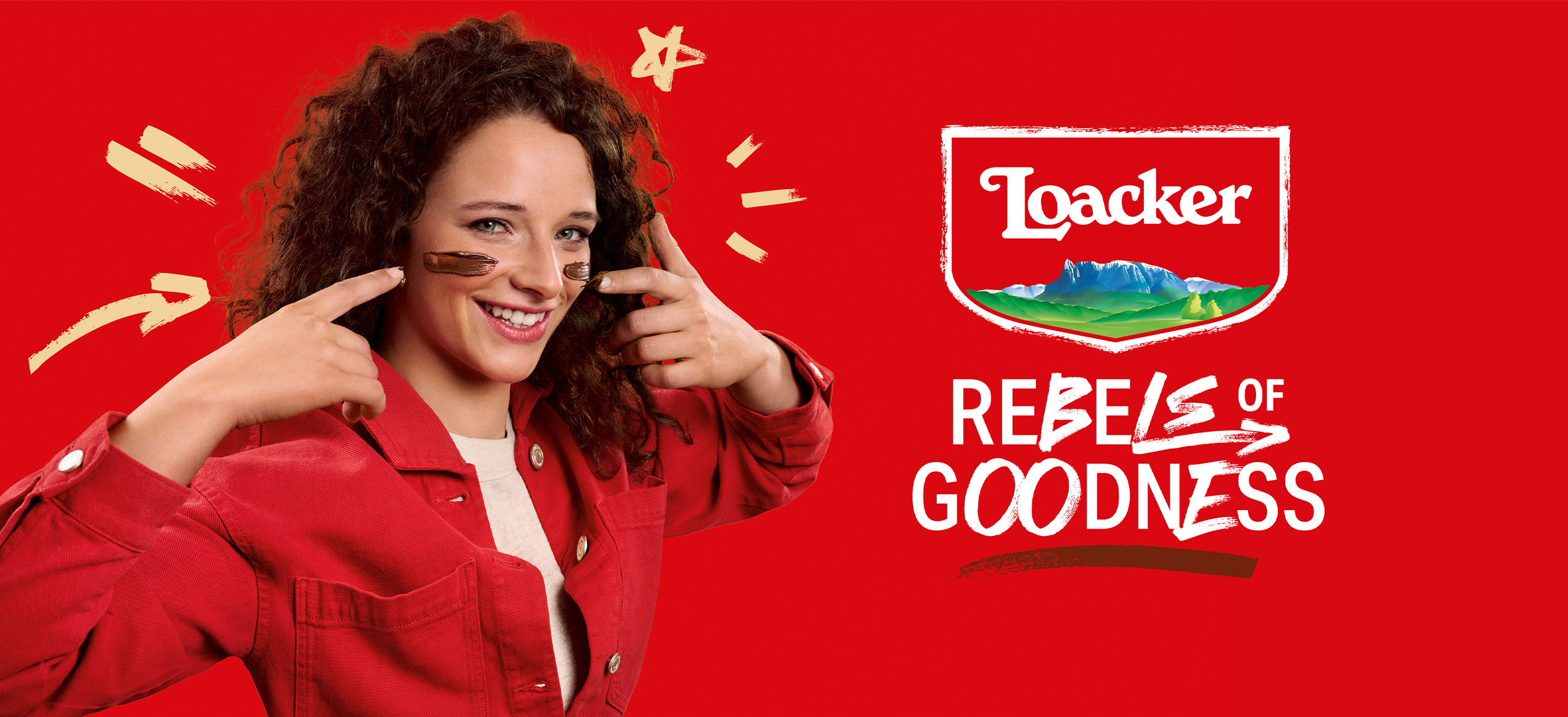Donna sorridente con cioccolato spalmato sulle guance in posa giocosa su sfondo rosso, accanto al logo Loacker e al claim
