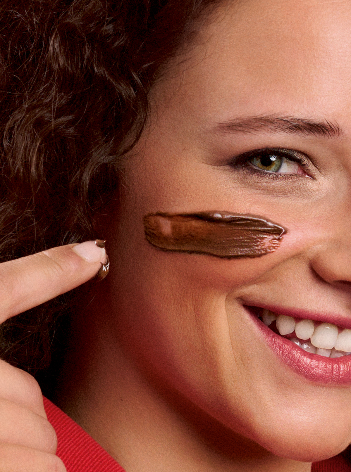 Primo piano della guancia di una donna sorridente con una striscia di crema al cioccolato stesa e un dito che la tocca