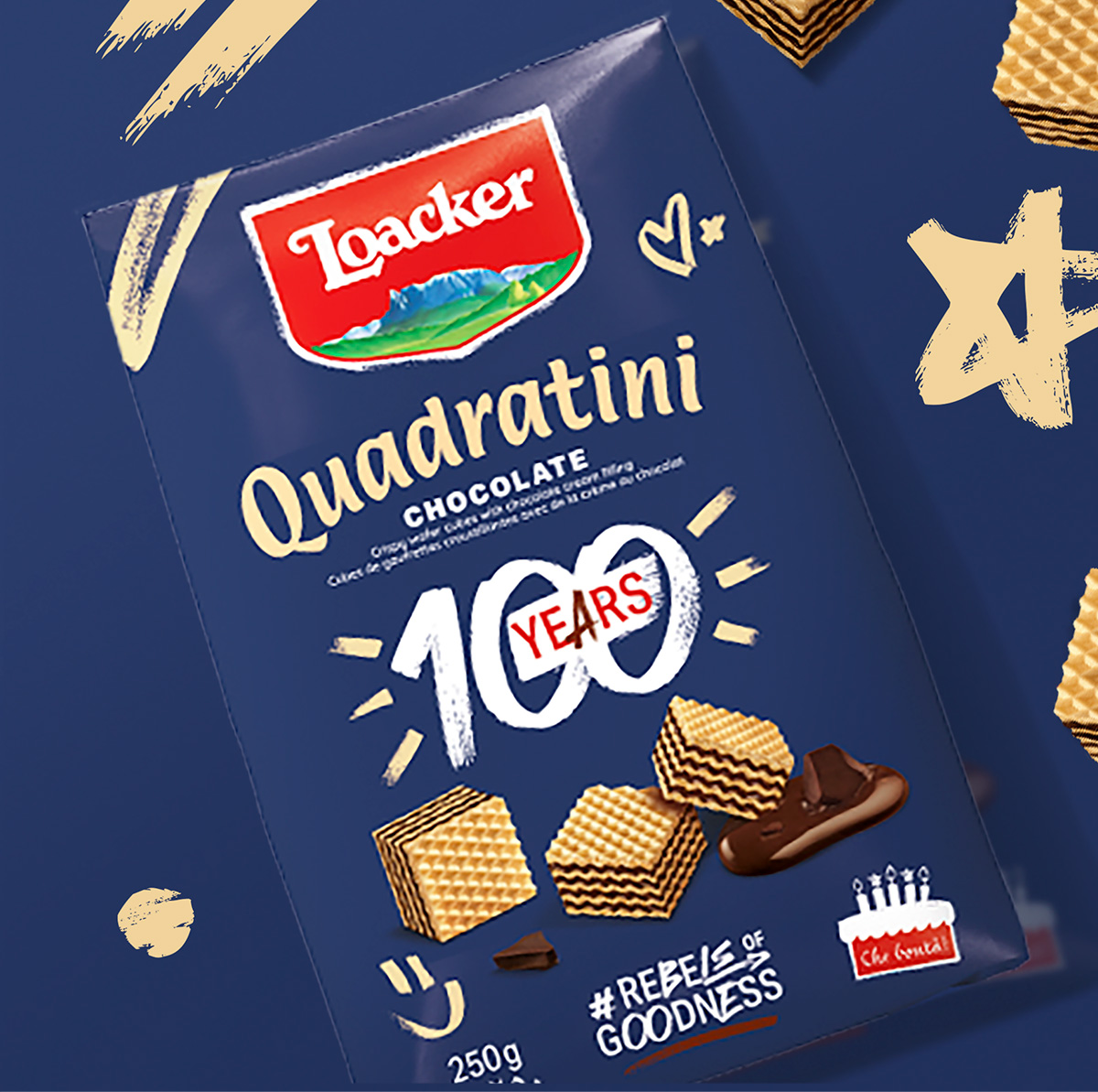 Confezione blu di Loacker Quadratini con scritta “100 Years”, decorata con simboli disegnati e cubetti di wafer al cioccolato